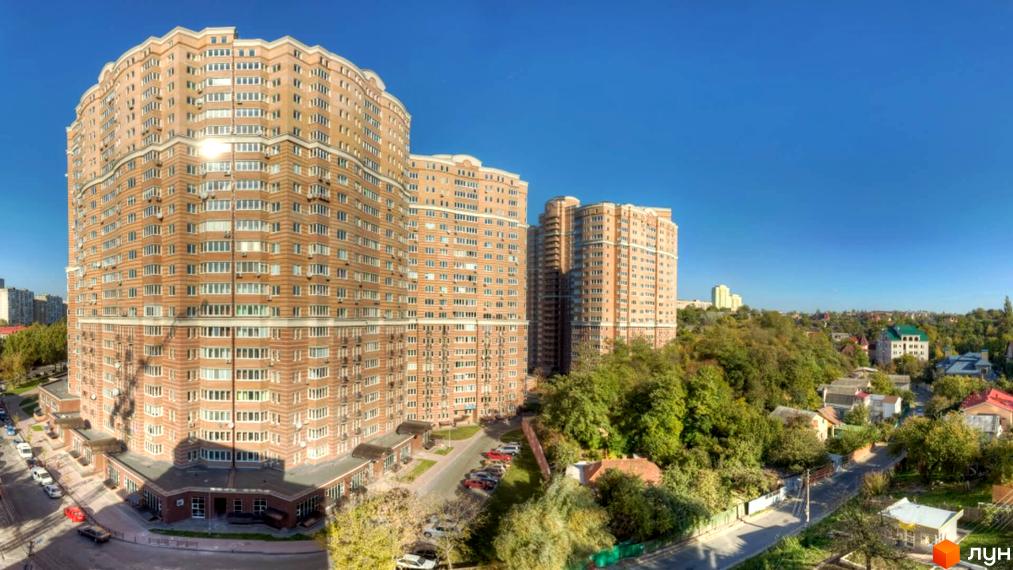 Багатоповерхові будинки Житлового комплексу Голосіїво зі світло-коричневими фасадами та хвилястим дизайном. Навколо зелені насадження та парковка.