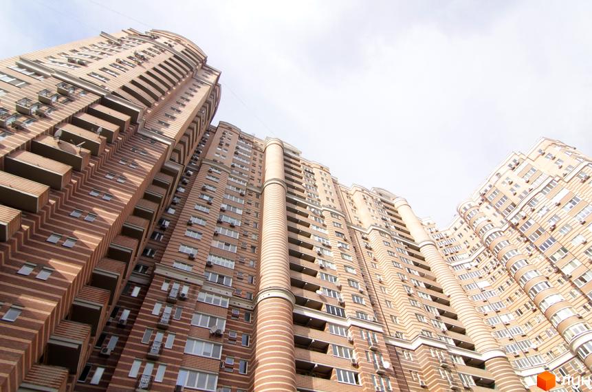 Житловий комплекс Голосіїво: високі будинки з коричнево-бежевим цегляним фасадом у смужку, вертикальні колони та безліч вікон і балконів.