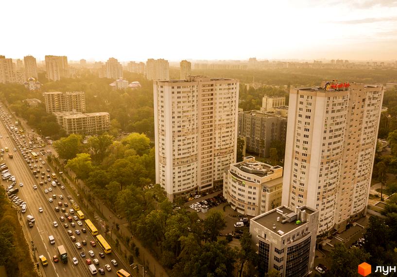 Високі багатоповерхові будинки Житлового комплексу Вікторія з численними вікнами, розташовані поруч з жвавою дорогою та зеленими насадженнями.