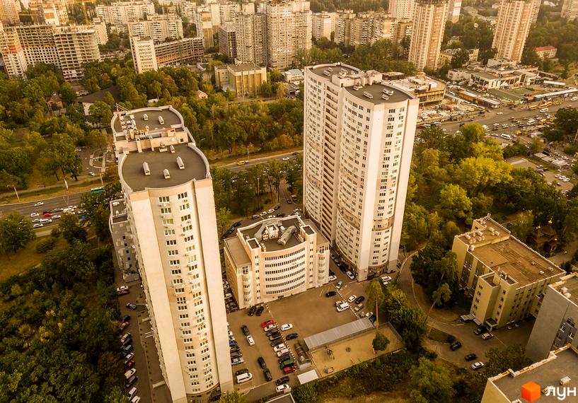 Аерофотографія Житлового комплексу Вікторія: два високі світлі будинки з округлими фасадами. Навколо зелені насадження та парковки.