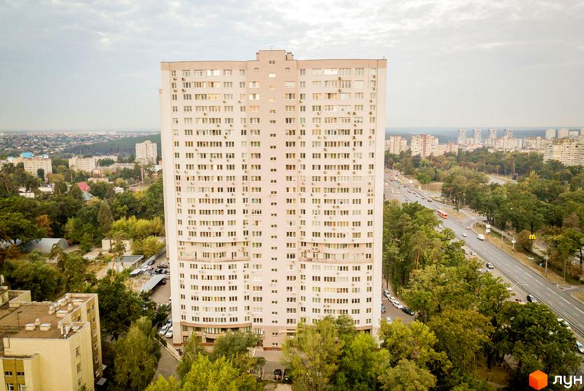 Житловий комплекс Вікторія: багатоповерховий будинок світлого кольору з численними вікнами, оточений зеленими насадженнями та міською інфраструктурою.