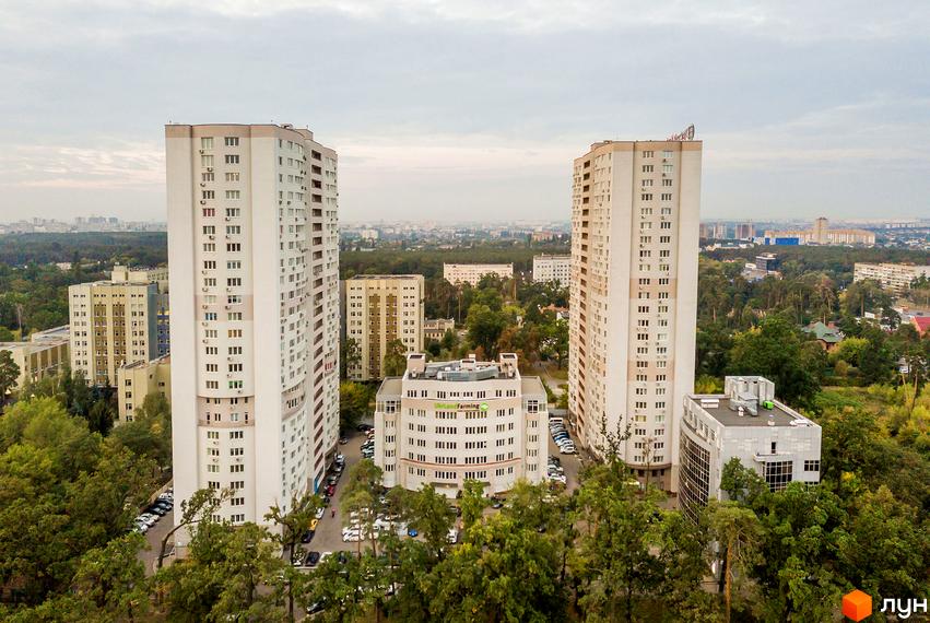 Два високі світлі будинки Житлового комплексу Вікторія з численними вікнами, оточені зеленими деревами та парковками.