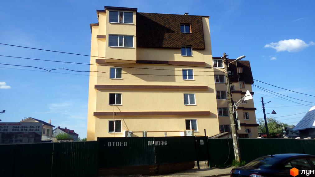 Житловий комплекс Осінній - це багатоповерховий будинок жовтого кольору з коричневими елементами та темним дахом. Навколо видно паркан та елементи прибудинкової території.