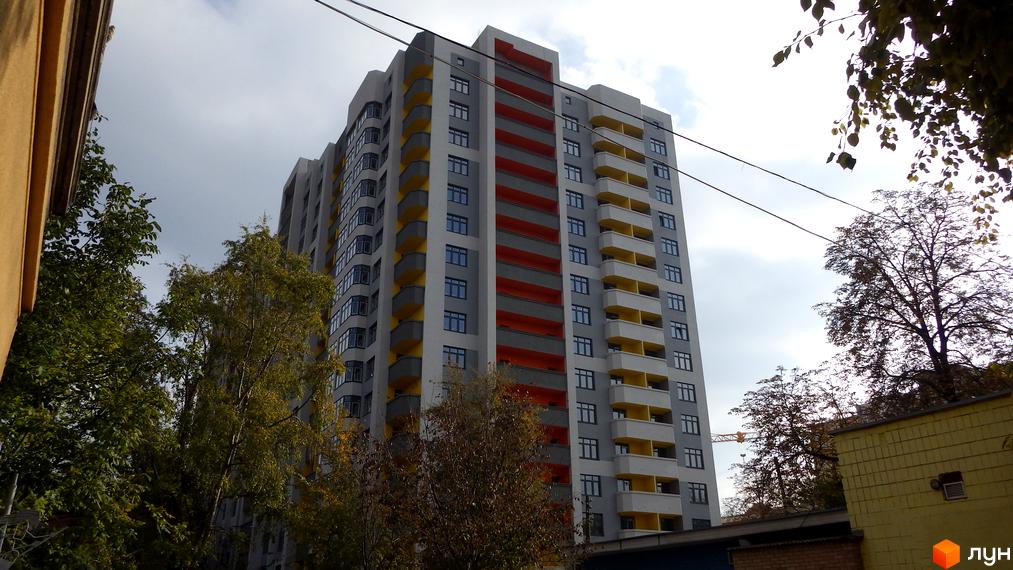 Житловий комплекс Наш будинок: багатоповерховий будинок із сірим фасадом, яскравими червоними та жовтими балконами, оточений деревами.