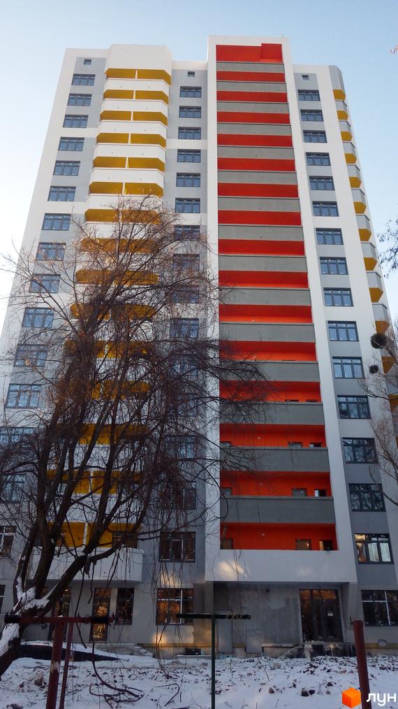 Житловий комплекс Наш будинок: багатоповерховий будинок з білим фасадом, сірими, жовтими та помаранчевими балконами. Зимовий пейзаж з деревами та снігом.
