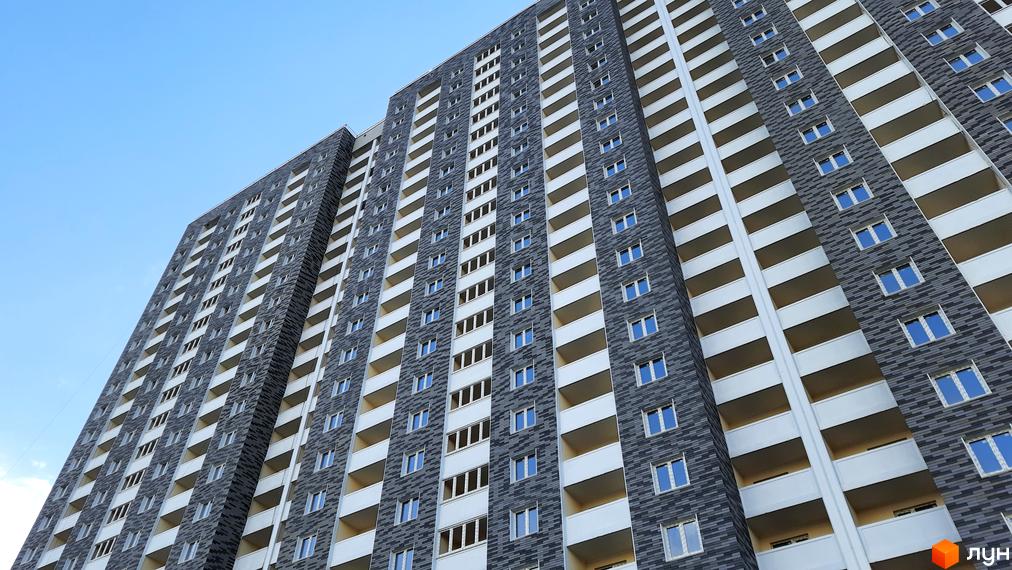 Зовнішній вигляд новобудови ЖК Ревуцький з численними балконами та вікнами на тлі блакитного неба. Будівельний проєкт з сірим фасадом та білими елементами.