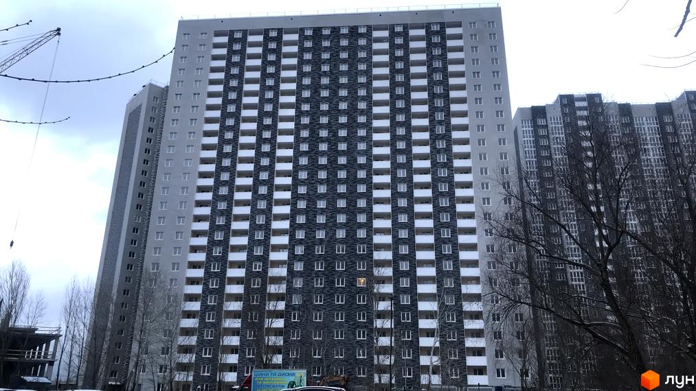 Зовнішній вигляд новобудови ЖК Ревуцький з сірими та темними фасадами, численними вікнами та балконами. Навколо видно дерева та будівельний кран.