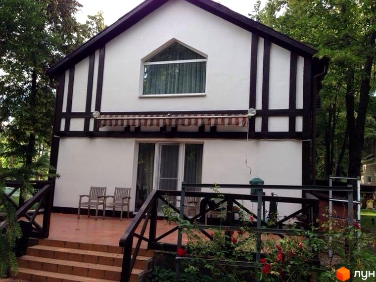 Будинок житлового комплексу КМ Иволга з білою фасадною частиною та дерев'яними елементами. Прибудинкова територія озеленена та облаштована.