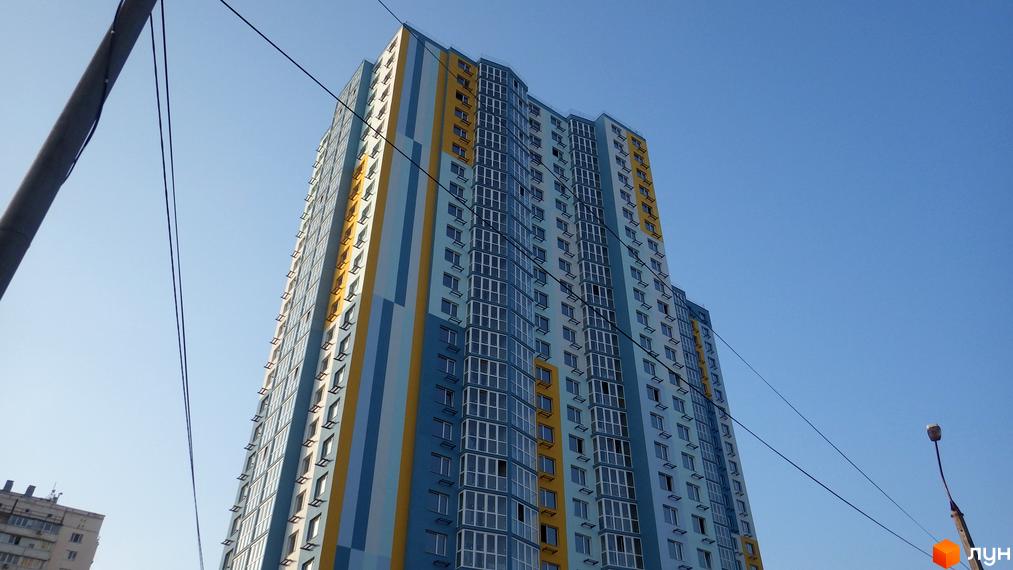 Новобудова ЖК Welcome Home на Ревуцького з блакитно-жовтим фасадом. Висотна будівля з численними вікнами та балконами на фоні ясного неба.