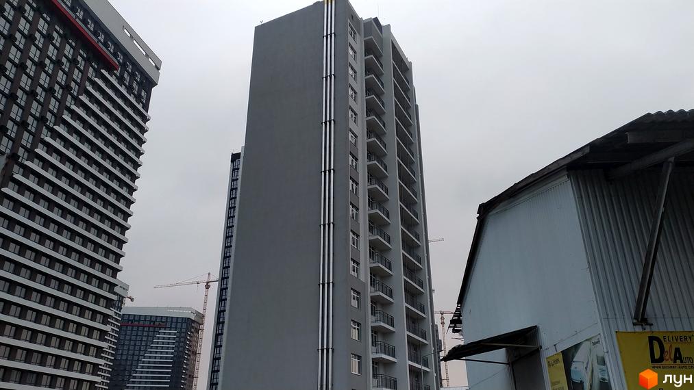 Сірі багатоповерхові будинки з балконами та вертикальними елементами на фасаді. На задньому плані видно будівельні крани.