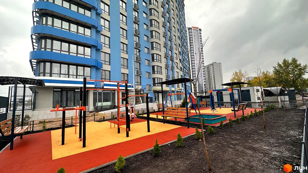 Житловий комплекс Берег Дніпра з блакитною фасадною обробкою та дитячим майданчиком з гойдалками та пісочницею.