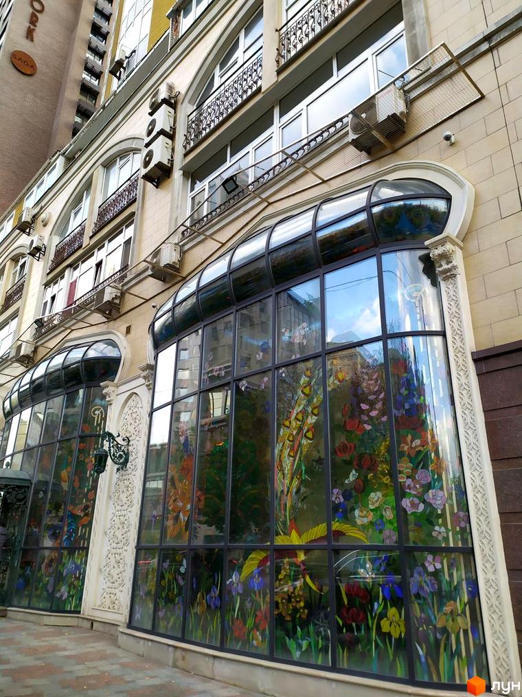 Зовнішній вигляд житлового комплексу на вул. Антоновича, 72 з великими вікнами та декоративними елементами. Прибудинкова територія оформлена зеленими насадженнями.