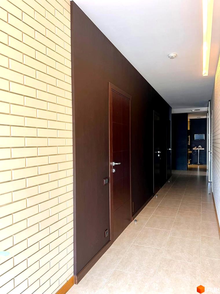Коридор житлового комплексу вул. Антоновича, 72 з світлими плитками та темними стінами. Вид на двері квартир та освітлення.