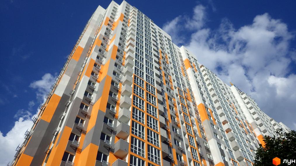 Зображення фасаду багатоповерхового будинку Житлового комплексу Пектораль на фоні блакитного неба з хмарами. Вигляд новобудови ззовні.