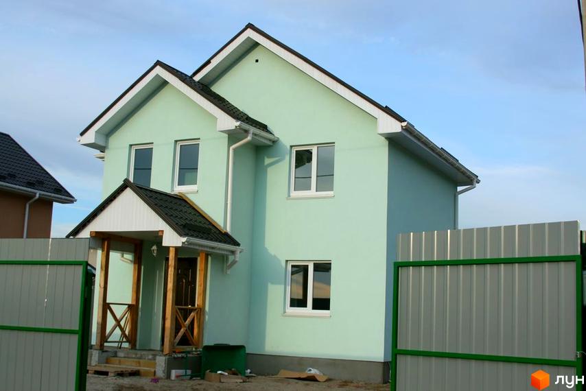 Зовнішній вигляд будинку в Котеджному містечку Лісна Пісня. Двоповерховий будинок з зеленими стінами та темним дахом, біля будинку сірий паркан.