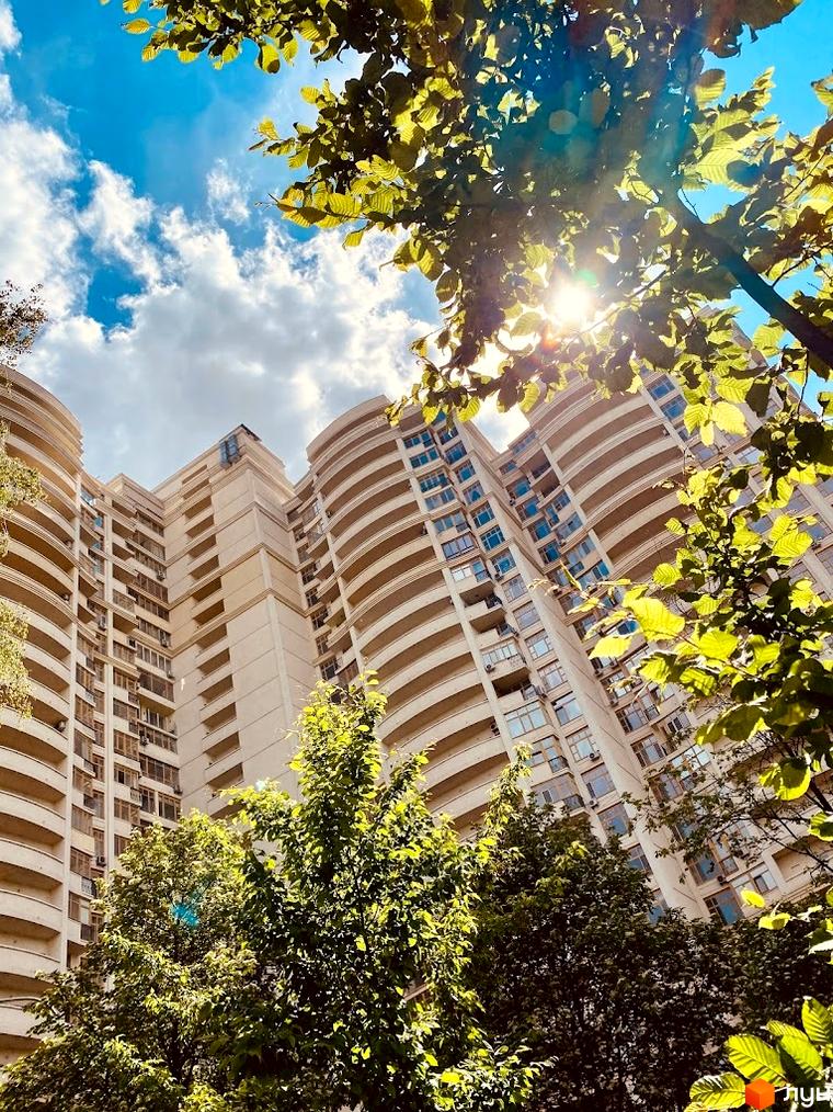 Житловий комплекс Golden Park з вигнутими балконами та світлим фасадом, оточений зеленими деревами під блакитним небом.