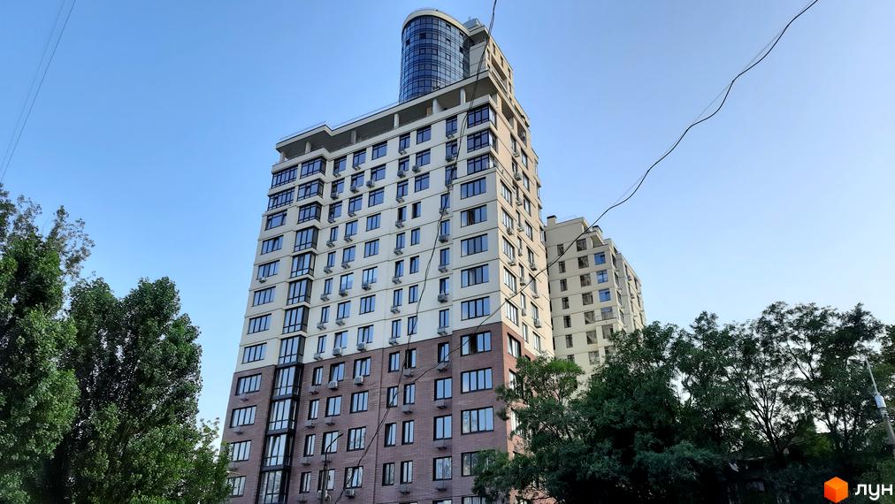Житловий комплекс Henesi House з сучасною архітектурою та великими вікнами. Прибудинкова територія озеленена деревами.