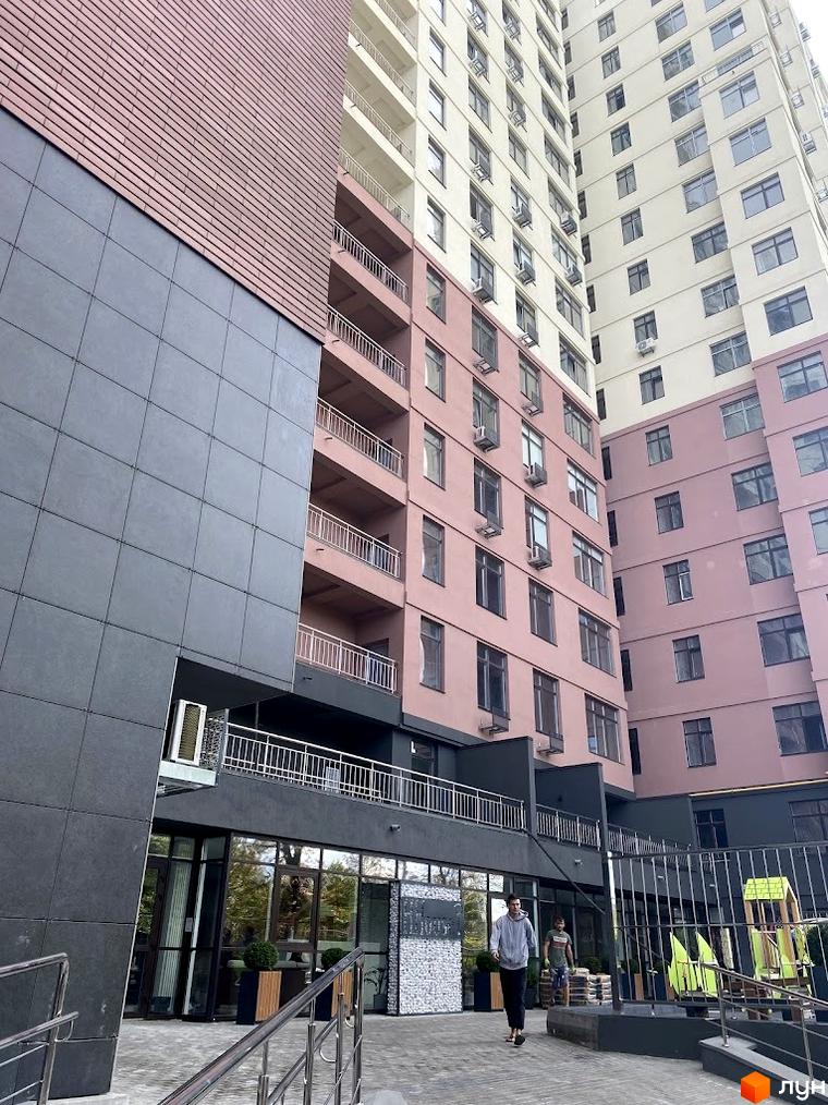 Житловий комплекс Henesi House з фасадом у світлих тонах та прибудинковою територією, що включає зони відпочинку.