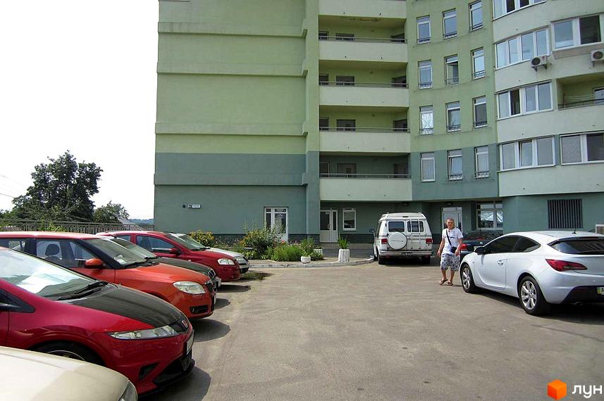 Житловий комплекс просп. Науки, 80а/73, з зеленими фасадами та прибудинковою територією, де припарковані автомобілі.