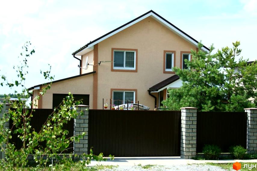 Фото будинку в Котеджному містечку Лісна Пісня. Двоповерховий будинок з коричневим парканом та цегляними стовпчиками.