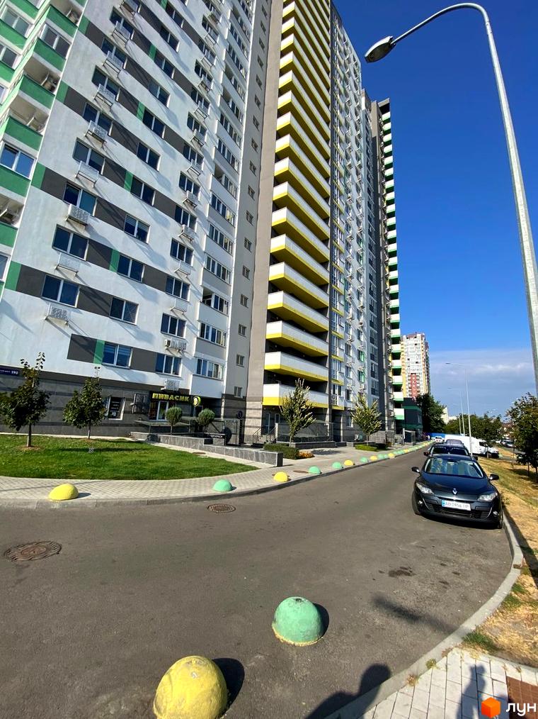 Зовнішній вигляд новобудови ЖК Харківський з яскравими жовтими та зеленими елементами. Прибудинкова територія з доглянутим газоном та дорогою.