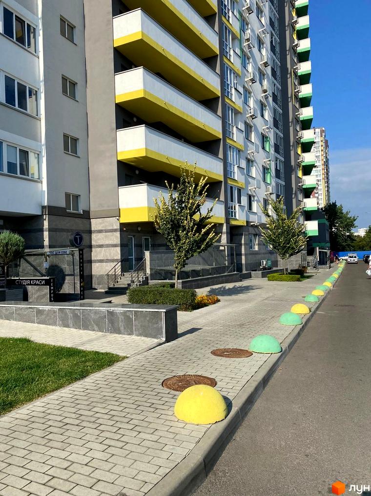 Зовнішній вигляд новобудови ЖК Харківський з жовтими балконами та прибудинковою територією з бруківкою та зеленими насадженнями.