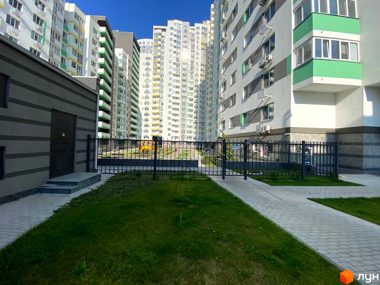 Зовнішній вигляд житлового комплексу Харківський з фасадами білого та зеленого кольору, що оточує доглянута прибудинкова територія з газоном та доріжками.