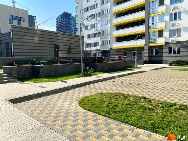 Новобудова ЖК Харківський: фасади будівель з жовтими елементами, прибудинкова територія з бруківкою та зеленими зонами.