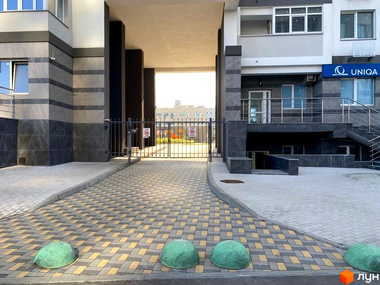 Зовнішній вигляд житлового комплексу Харківський з в'їзною брамою та бруківкою. Прибудинкова територія з зеленими напівсферами.