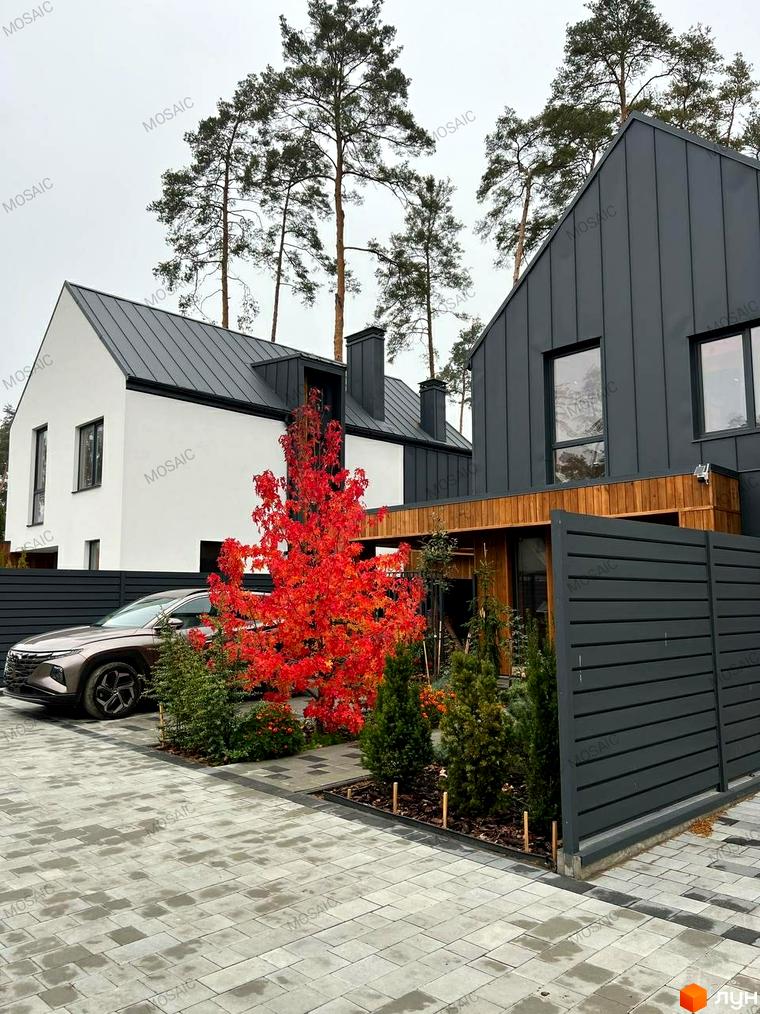 Котеджне містечко Toscana House 2: двоповерховий будинок з сірим фасадом, чорним дахом та червоним деревом на прибудинковій території. Поруч припаркований автомобіль та вимощена бруківкою доріжка.