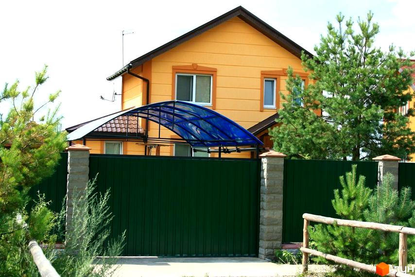 Фото будинку в Котеджному містечку Лісна Пісня. Двоповерховий будинок з жовтими стінами, зелений паркан та доглянута територія.