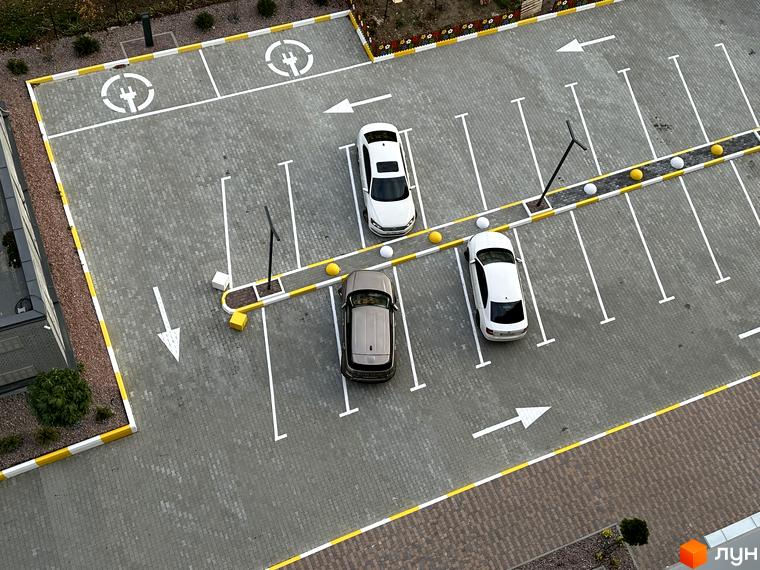 Паркінг біля новобудови ЖК Всі Свої з позначками для електромобілів. На парковці розташовані три автомобілі та розмітка для паркомісць.