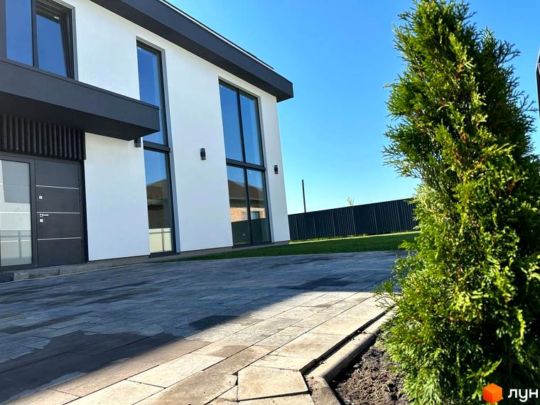 Зовнішній вигляд будинку КМ PARK by berezivka з великими вікнами та сірими дверима, прибудинкова територія з бруківкою та зеленим газоном.