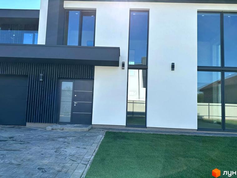 Котеджне містечко КМ PARK by berezivka. Фасад будинку з великими вікнами та темними елементами, прибудинкова територія з газоном та вимощеною доріжкою.