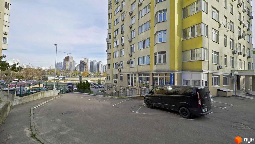 Зовнішній вигляд багатоповерхового будинку на вул. Саперно-Слобідська, 24. Прибудинкова територія з парковкою та зеленими насадженнями.