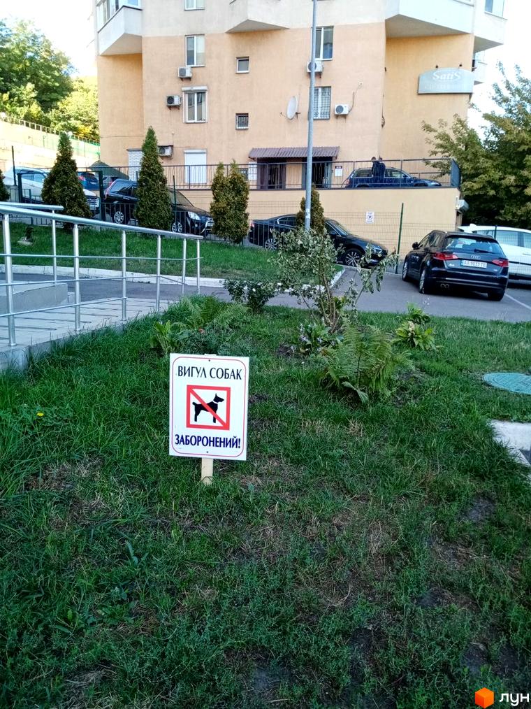 Житловий комплекс на вул. Саперно-Слобідська, 24. Зовнішній вигляд будівлі та прибудинкова територія з газоном та знаком заборони вигулу собак.