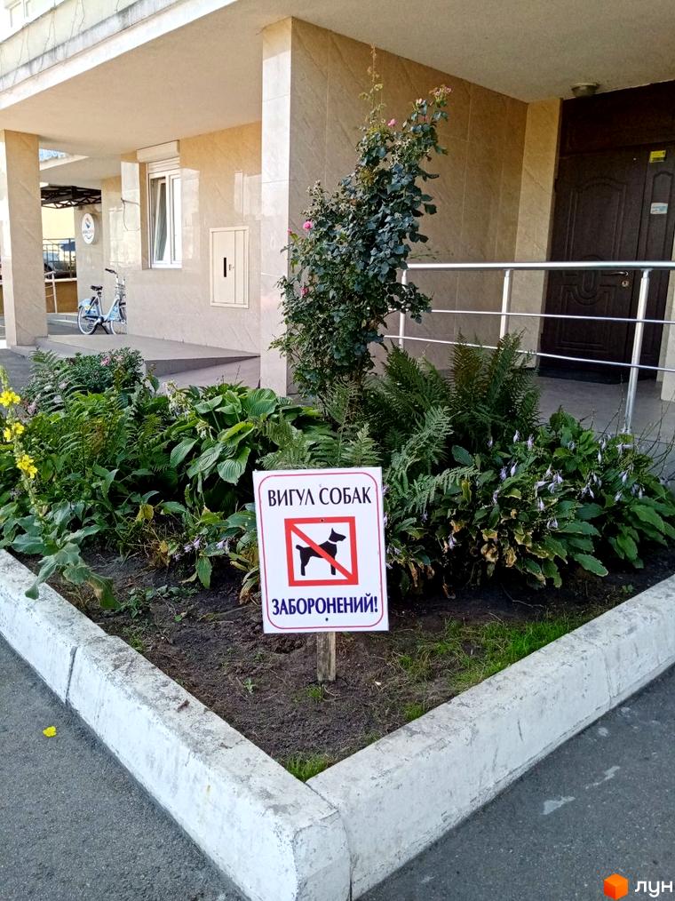 Житловий комплекс Саперно-Слобідська, 24. Зовнішній вигляд будинку та прибудинкова територія з клумбою та знаком заборони вигулу собак.