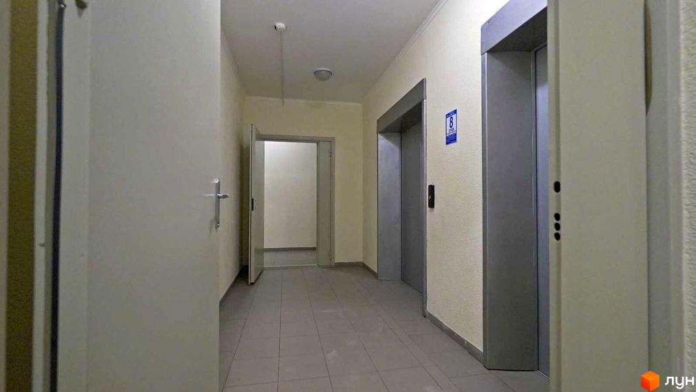 Коридор з дверима та ліфтом у житловому комплексі на вулиці Саперно-Слобідській, 24. Оздоблення стін та підлоги в нейтральних тонах.