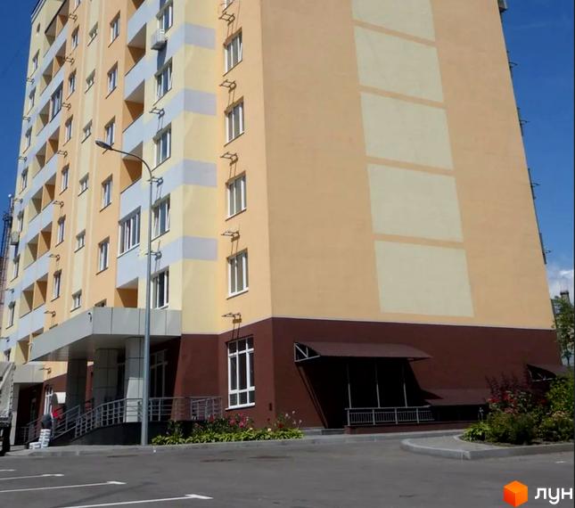 Клубний будинок Gelios – це багатоповерхова новобудова з фасадом у світлих тонах та коричневим цоколем. Перед будинком облаштований паркінг та зелена зона.