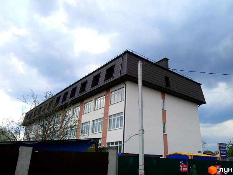 Клубний будинок Весна на вулиці Осінній – це чотириповерхова новобудова з мансардним дахом та великою кількістю вікон. Навколо будинку розташована огорожа та дерева.