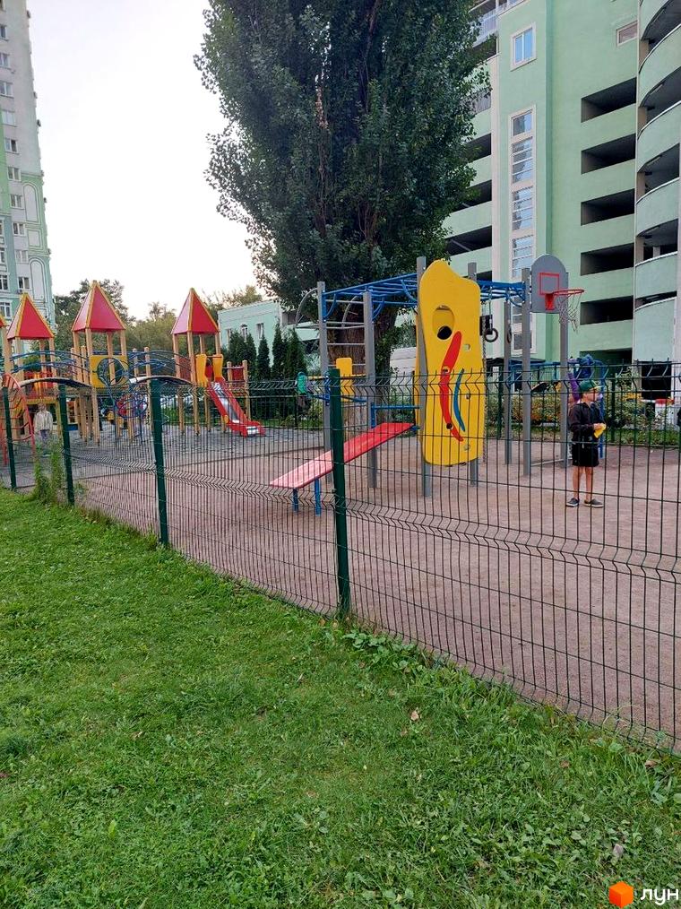 Багатоповерховий будинок Житлового комплексу Паркові озера. На передньому плані дитячий майданчик з яскравими ігровими елементами та огорожею.
