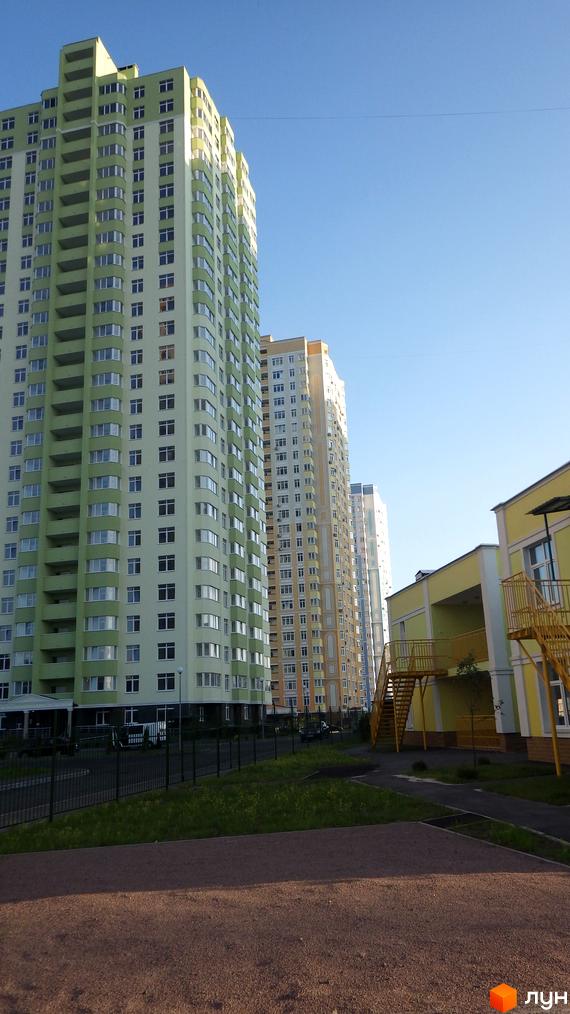 Житловий комплекс Паркові озера: багатоповерхові будинки світло-зеленого та жовтого кольорів. Видно прибудинкову територію з огорожею, газоном та жовтою будівлею.