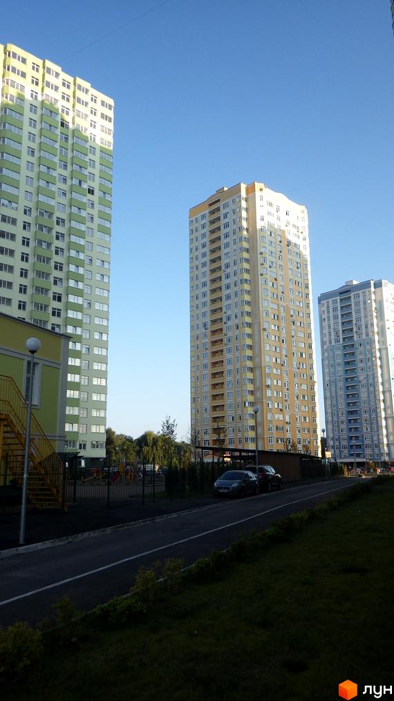 Житловий комплекс Паркові озера: висотні будинки світло-зеленого, бежевого та блакитного кольорів. Видно дорогу, газони та дитячий майданчик.