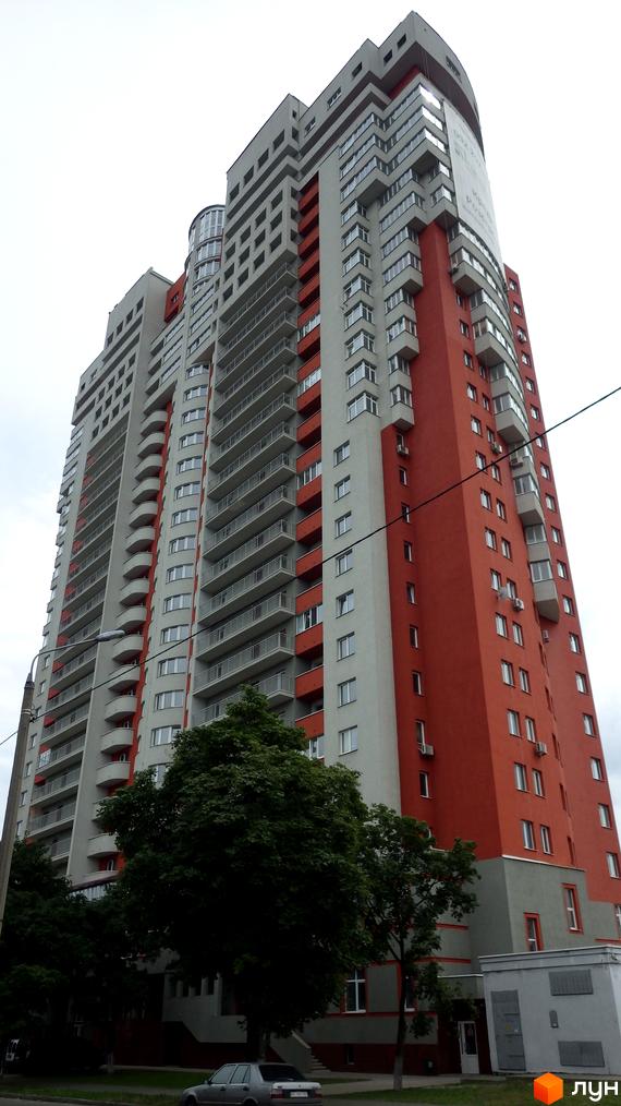 Високий Житловий комплекс Воскресенський з фасадом у червоних та світло-сірих тонах, численними балконами. Перед будинком ростуть дерева та проходить дорога.