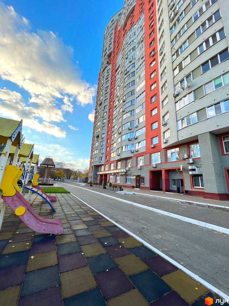Житловий комплекс Воскресенський з сірим та червоним фасадом. На передньому плані дитячий майданчик з гірками та кольоровою плиткою, поруч доріжка.