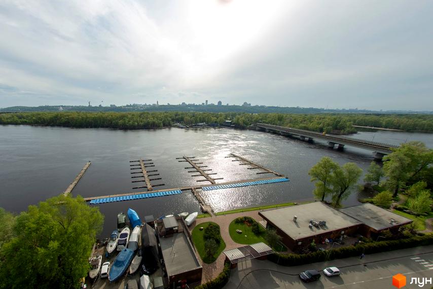 Будівлі Житлового комплексу Рів'єра Ріверсайд з плоскими дахами та темними фасадами. Поруч річка з причалами для човнів, мостом та зеленою зоною.