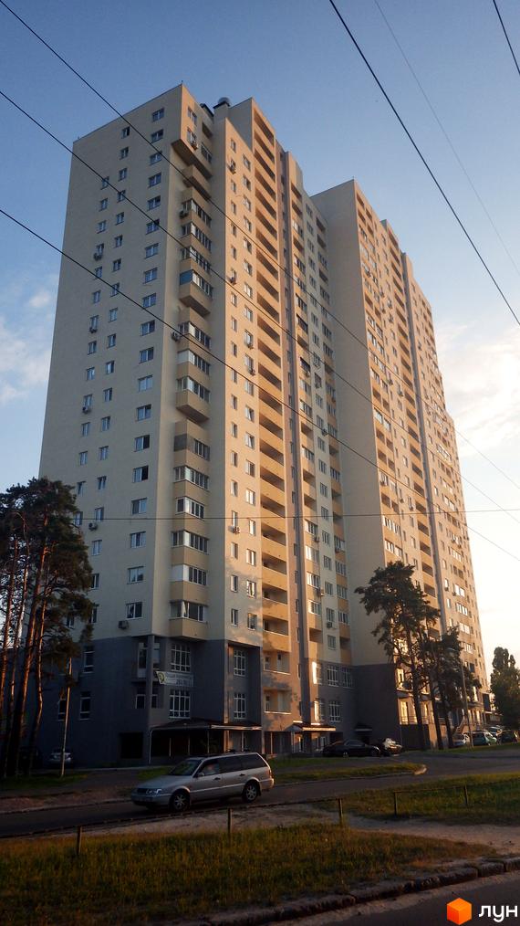 Житловий комплекс Перовський з високими будинками та прибудинковою територією, оточений деревами та автомобілями.