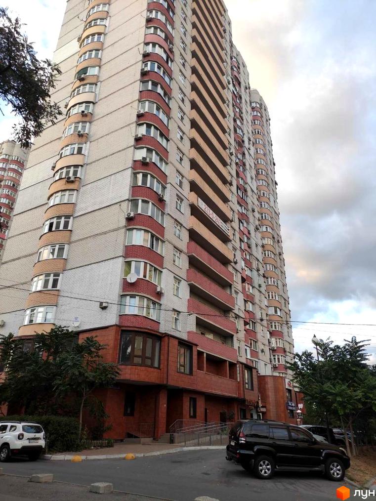 Житловий комплекс на вул. Петра Калнишевського, 7. Вид на фасад будинку та прибудинкову територію з автомобілями та зеленими насадженнями.