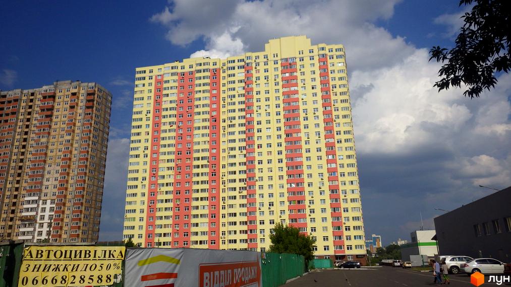Житловий комплекс Яскравий у Києві. Зовнішній вигляд будівель: жовті та червоні фасади, багато вікон. Прибудинкова територія: дорога, дерева, припарковані автомобілі.
