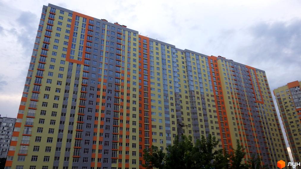 Зовнішній вигляд житлового комплексу ЖК Яскравий з яскравими фасадами жовтого та сірого кольорів з помаранчевими елементами. Висотна будівля з численними вікнами та балконами.